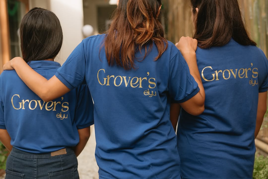 Three Grover's Elyu staff members in branded blue shirts, backs to camera, property exterior in background
