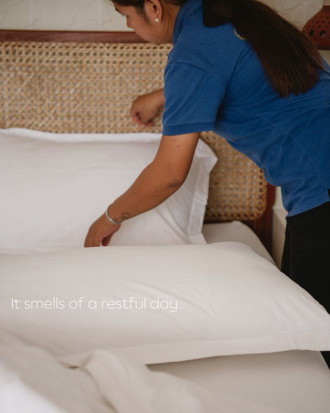 Grover's staff member arranging fresh white pillows on a bed with rattan headboard